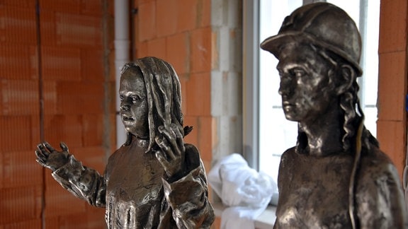 Die Gesichter zweier Skulpturen: ein Bergmann mit Helm und ein Engel mit Down-Syndrom. 