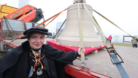 Gerd Schlesinger, Vorsitzender des Vereins Friedensglocke Fichtelberg, steht neben der neuen Friedensglocke für den Fichtelberg, die zur Weihe auf einem Transporter auf dem Fichtelberg steht.