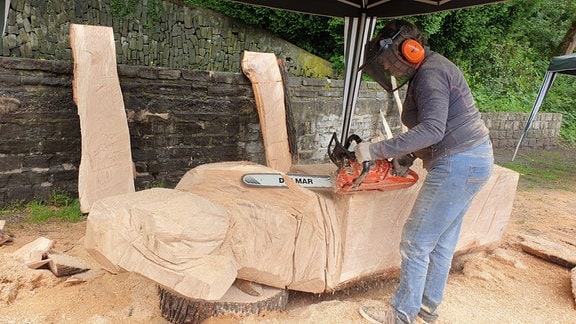Eine Frau bearbeitet mit einer Motorsäge einen Holzstamm.