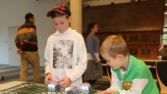 Zwei Jungen probieren an einem Tisch einen Käferroboter aus.