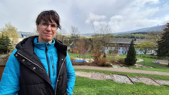 Die Leiterin des Kindergartens "Regenbogen", Sylvia Weißbach steht im Garten der Einrichtung. Im Hintergrund sieht man den Klínovec (Keilberg) auf tschechischer Seite.