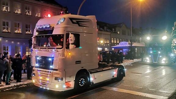 Lastkraftwagen mit weihnachtlicher Beleuchtung auf Straße. Zuschauer am Straßenrand.
