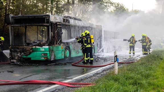Feuerwehrleute löschen einen brennenden Bus. 