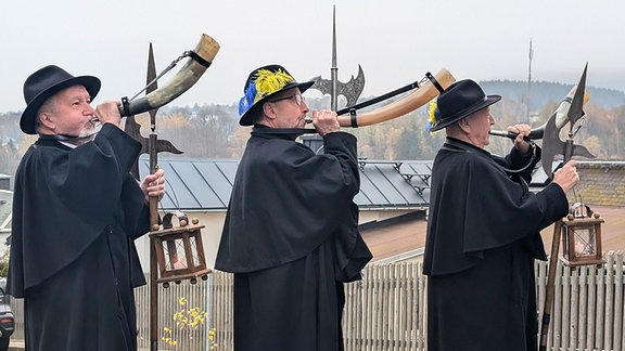 Drei Männer in Nachtwächtergewand stoßen ins Horn.