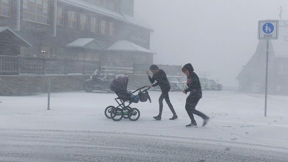 Zwei Frauen laufen durch starkes Schneetreiben. Eine der Frauen schiebt einen Kinderwagen.