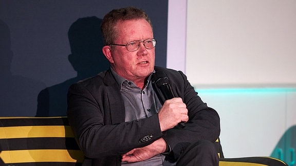 Gerd Lippold, Staatssekretär im Sächsischen SEKUL auf einem Podium mit Mikrofon.