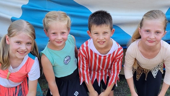 Vier Kinder einer Grundschule haben Zirkuskostüme an, sind geschminkt und freuen sich auf ihren Auftritt in der Manege.