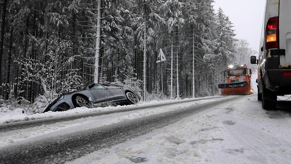 Ein Auto steht nach einem Unfall neben der schneebedeckten Fahrbahn im Graben, während ein Räumfahrzeug angefahren kommt.