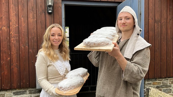 Eine junge Frau und ein junger Mann stehen in historischen Kostümen mit Stollen vor dem Bergwerkseingang "Im Gößner"