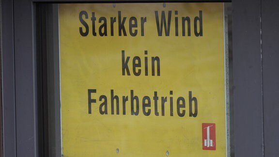 Auf einem großen gelben Schild steht in schwarzen Buchstaben gedruckt: Starker Wind - Fahrbetrieb eingestellt. Das Schild hing am 3.8.2023 am Eingang der Fichtelbergbahn in Oberwiesenthal in Sachsen.