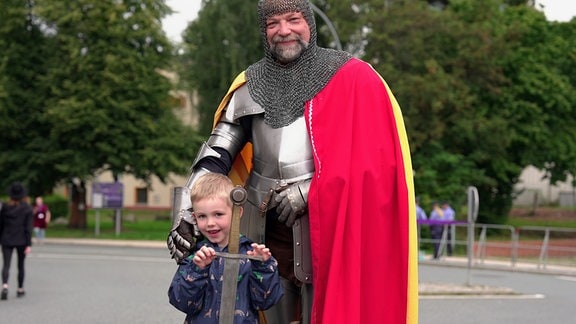 Ein kleiner Junge steht neben einem bärtigen, großen Mann in Ritterrüstung. Der Mann stellt Ritter Georg aus Schwarzenberg dar.