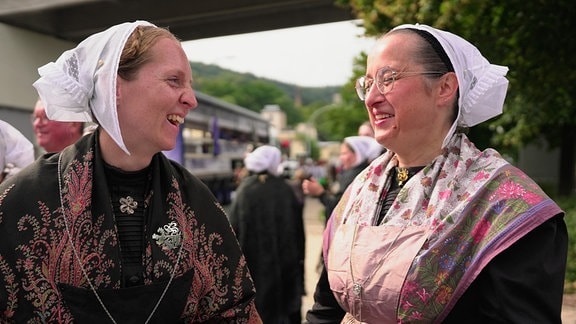 Zwei Frauen mittleren Alters haben dunkle Trachten an und stehen nebeneinander. Die beiden stammen aus der Bretagne in Frankreich und sind als Gäste der Partnerstadt Aue nach Sachsen gekommen.
