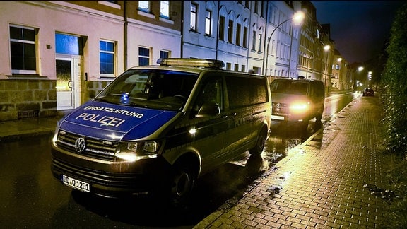 Am Straßenrad stehen zwei Polizeifahrzeuge vor Mehrfamilienhäusern im Regen.