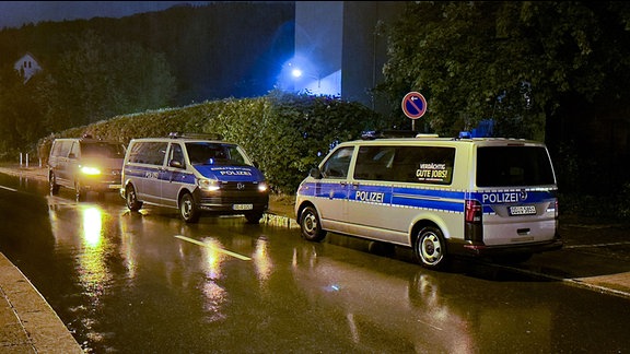 Drei Polizeifahrzeuge stehen auf einer regennassen Straße am Straßenrand.