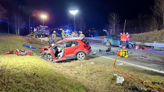 Eine von der Feuerwehr ausgeleuchtete Unfallstelle mit zwei zerstörten Fahrzeugen links und rechts im Straßengraben