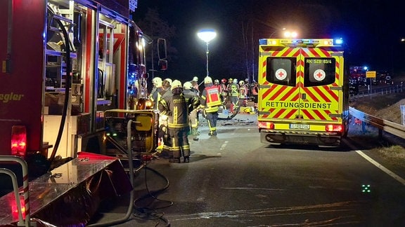 Zwischen einem Feuerwehr- und einem rettungsfahrzeug stehen viele Einsatzkräfte an einer Unfallstelle.