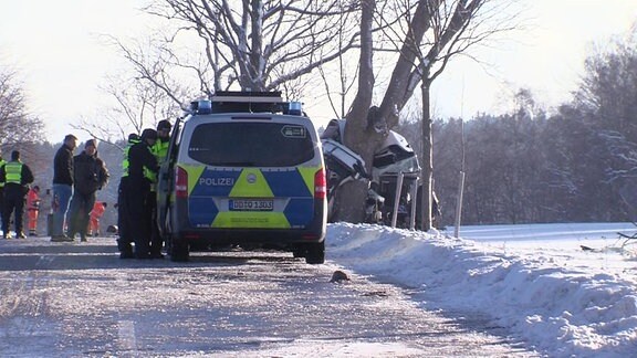 Menschen in Warnkleidung und ein Polizeiauto stehen an einem winterlichen Tag auf einem Weg.