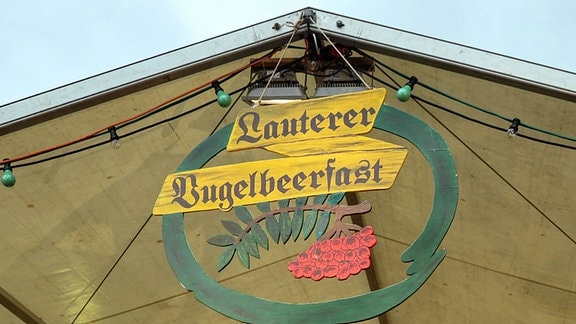  An dem Dach eines Festzeltes hängt ein Holzschild mit der Aufschrift Lauterer Vugelbeerfast. 