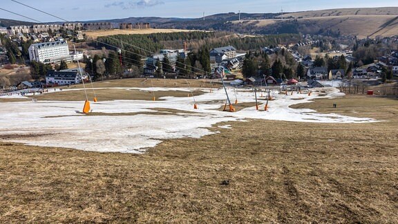 In einem Mittelgebirge sieht man Berghänge mit viel braunem Boden, nur an einzelnen Stellen liegt noch Schnee, der Skipisten erahnen lässt. Die Skilifte am hnag rugen. Der Betrieb wurde eingestellt.