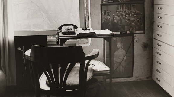 Gerdi Sippel: Gerhard Klampäckel, Atelier VI, 1979, Schwarz-Weiß-Foto eines Zimmers, in dem ein Schreibtisch mit Stuhl vor einem Fenster steht, hinter dem ein winterlich-kahler Baum zu sehen ist.