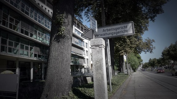 Ein Hinweisschild mit der Aufschrift "Arbeitsgericht, Verwaltungsgericht" weist auf die Funktion der an einer großen Straße befindlichen Bürokomplexe hin