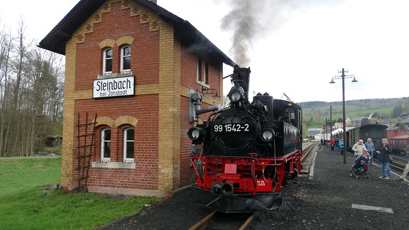 Schöne alte Dampflok steht direkt neben sehr kleinem Bahnhofhäusschen, das mit "Steinbach bei Jöhstadt" beschildert ist