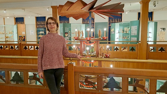 Sybille Gluch, Leiterin des Erzgebirgischen Spielzeugmuseums Seiffen, steht an einem Geländer vor einem Leuchter.