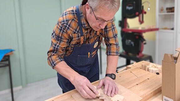An einer Holzwerkbank arbeitet ein Mann und ist halb gebückt und konzentriert bei der Arbeit.