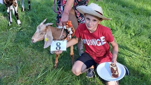 Eine Frau und ein Junge präsentieren eine geschmückte Ziege auf einer Wiese.