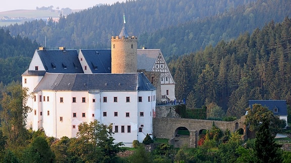 Burg Scharfenstein mit weißer Fassade ist umgeben von Wald