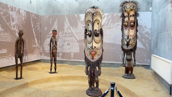 Vier überlebensgroße geschnitzte Figuren aus Ozeanien stehen auf einer Ausstellungsfläche. 