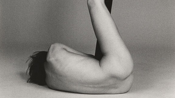 Eine am Boden liegende nackte Frau streckt ihr Bein an einer schrägen Stange hoch.