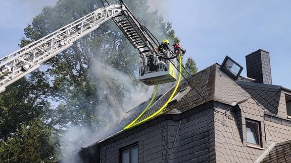 Die Feuerwehr Chemnitz fährt einen Drehkran ans Dach eines doppelhaushälfe heran. Feuerwehrleute versuchen, den Qualm und ein Feuer zu löschen.