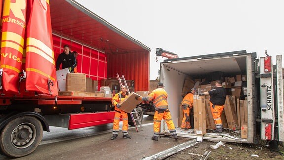 Männer laden Pakete aus dem verunglückten Lkw in einen anderen Lastwagen.