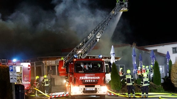 Feuerwehrleute löschen von einem Drehleiterfahrzeug das brennende Dach einer Gaststätte.