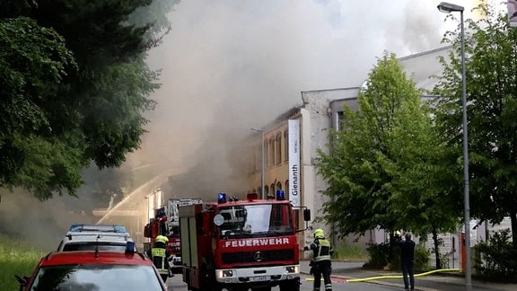 Eine Halle steht in Flammen, viele Feuerwehrautos davor.