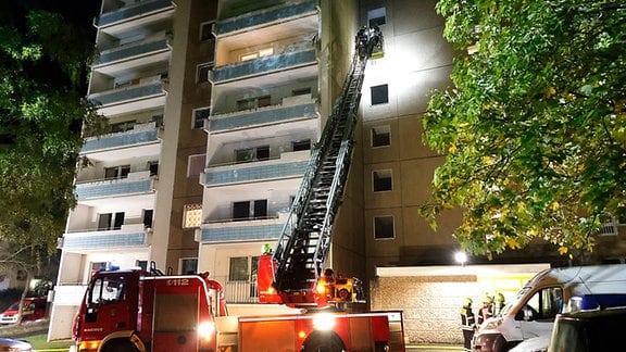 Ein Feuerwehrauto mit Leiter steht an einem Hochhaus.