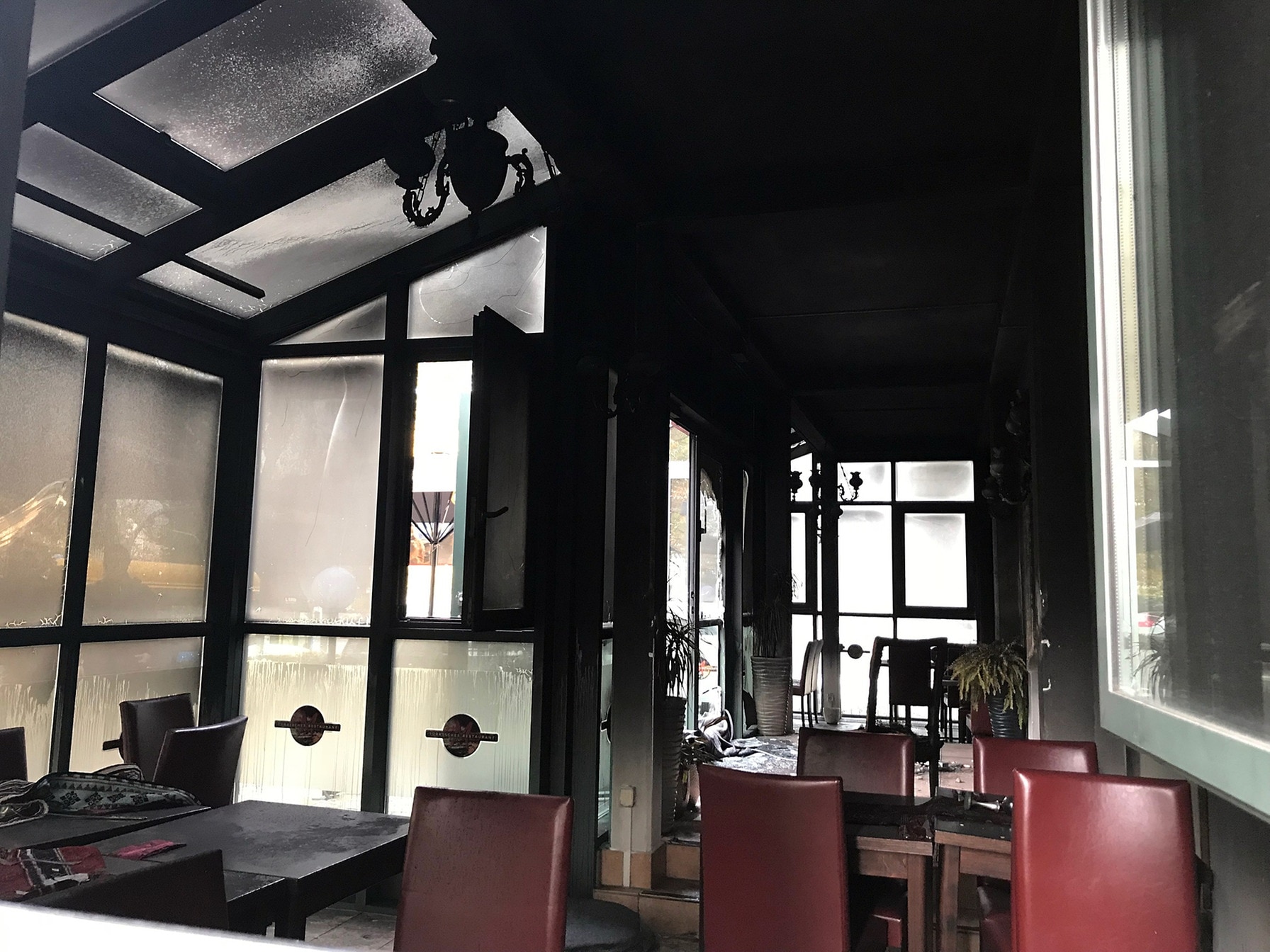 Blick in einen verrussten Wintergarten eines Restaurants mit deutlichen Brandspuren