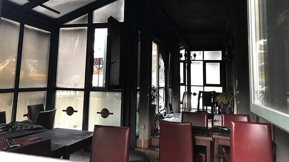 Blick in einen verrussten Wintergarten eines Restaurants mit deutlichen Brandspuren