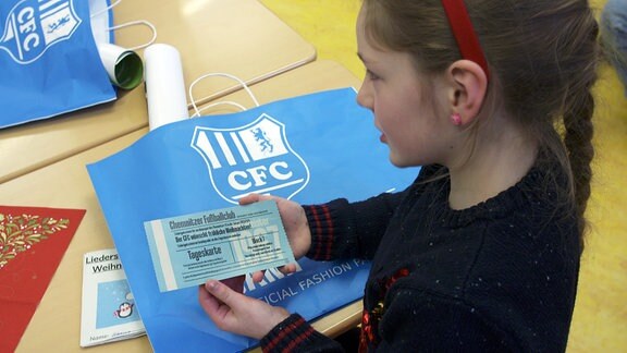 Eine Grundschülerin zeigt eine Tageskarte für den CFC in die Kamera.