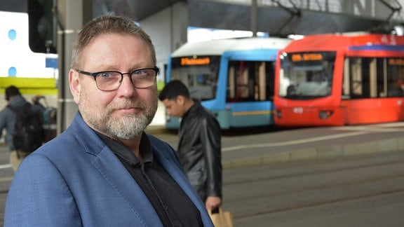 Falk Ester, Pressesprecher der City-Bahn Chemnitz, steht vor zwei Straßenbahnen im Bahnhof.