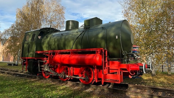 Eine restaurierte grüne Lokomotive mit rotem Fahrgestell ohne Schornstein steht auf einem Abstellgleis.