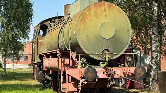 Eine alte Lokomotive mit verblasstem Anstrich und Rostspuren steht auf einem Abstellgleis.