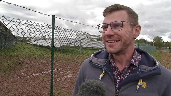 Der Bürgermeister von Neukirchen, Sascha Thamm, steht am Zaun vor einem Solarpark