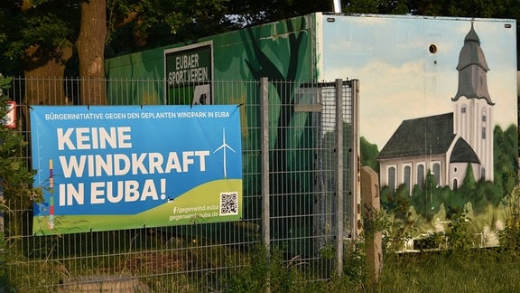 An einem Zaun hängt ein Plakat "Keine Windkraft in Euba!".