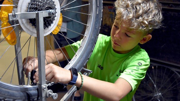 Ein Junge zieht die Speichen an einem Rad in einem Zentrierständer an.