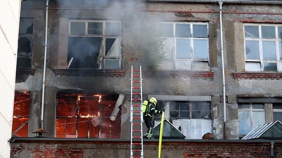 Ein Gebäude brennt, ein Feuerwehrmann steht an einer Leiter.