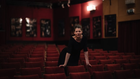 Eine Frau steht im Theater zwischen Sitzreihen mit rotem Samt.
