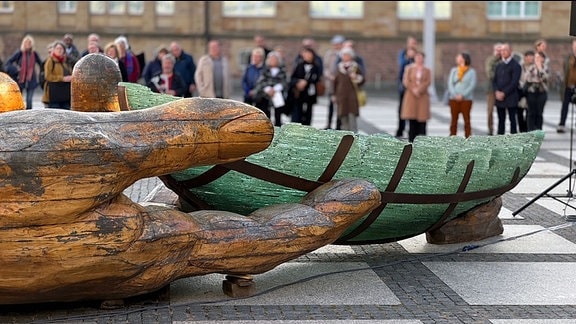 Eine Skultur liegt auf dem Chemnitzer Theaterplatz: Eine hölzerne Hand hält eine Schiff aus Glas. 