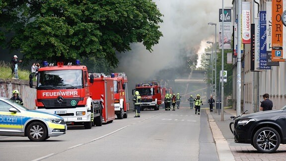 Feuerwehrfahrzeuge stehen in einer Straße unter schweren Rauchwolken..